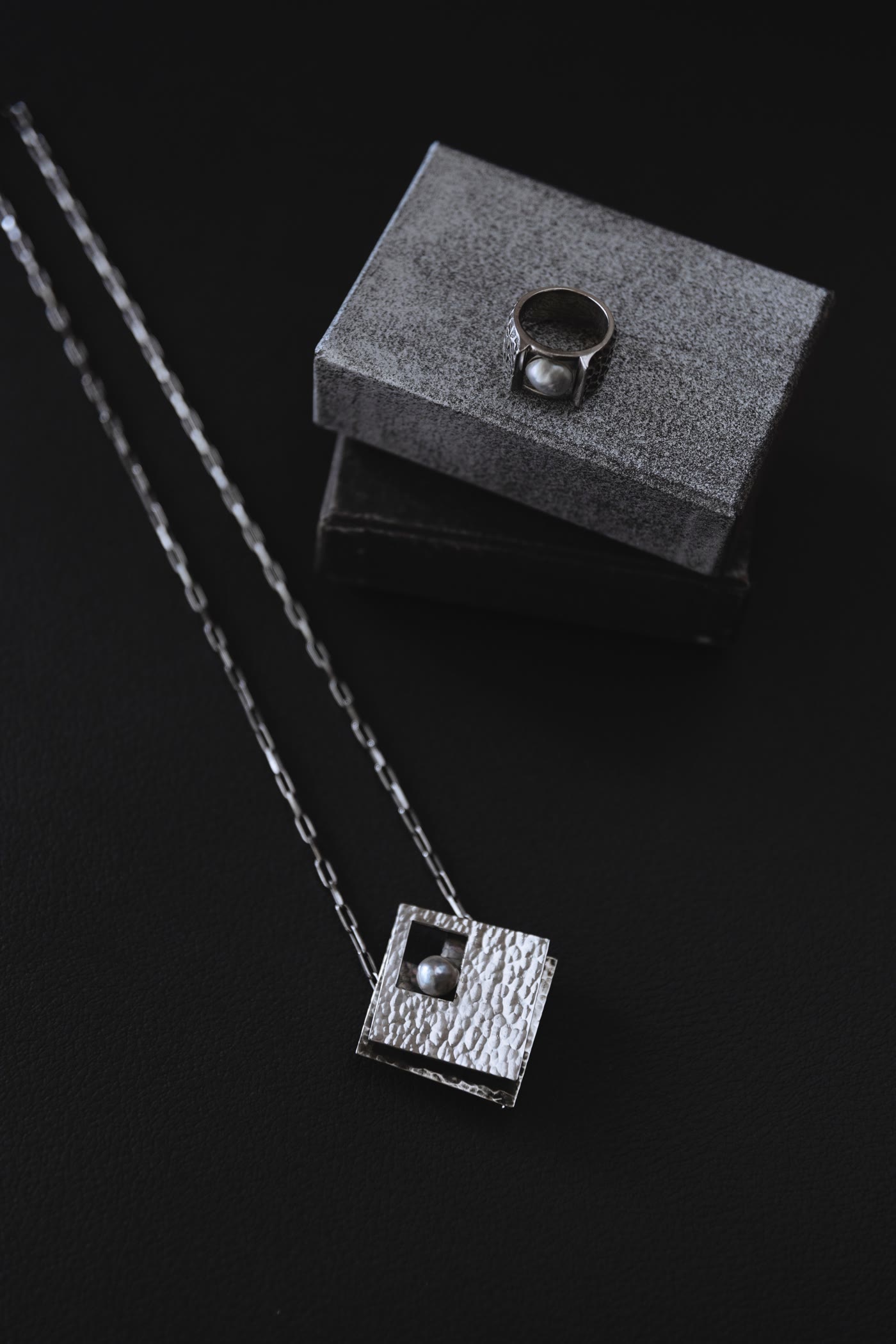 Pearl ring detail with a silver pendant on dark leather